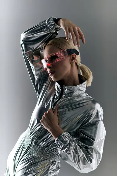Mujer extravagante con gafas futuristas en traje plateado haciendo movimientos robóticos y mirando hacia otro lado - foto de stock