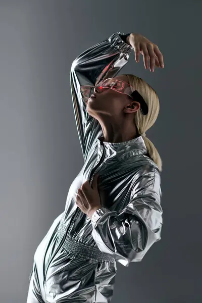 Mulher extravagante com óculos futuristas em traje de prata fazendo movimentos robóticos e olhando para longe — Fotografia de Stock