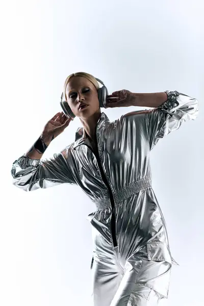Attraente bizzarro modello femminile con le cuffie che indossano abbigliamento robotico argento e godersi la musica — Foto stock