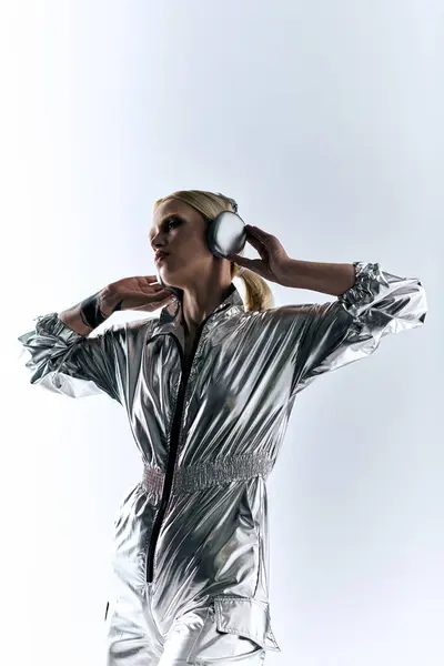 Екстравагантна красива жінка з сучасними навушниками в футуристичному срібному вбранні насолоджується музикою — стокове фото