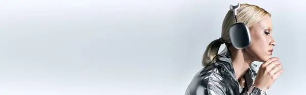 Приваблива жіноча модель з навушниками в срібному роботизованому одязі і насолоджується музикою, банером — стокове фото