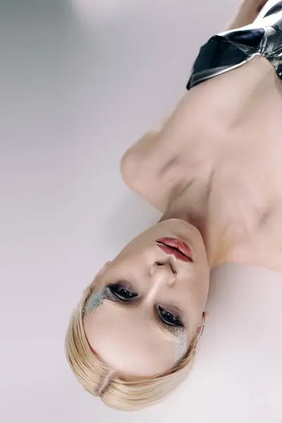 Futuristisch attraktive Frau mit blonden Haaren in silberfarbenem bizarrem Gewand liegt und blickt in die Kamera — Stockfoto