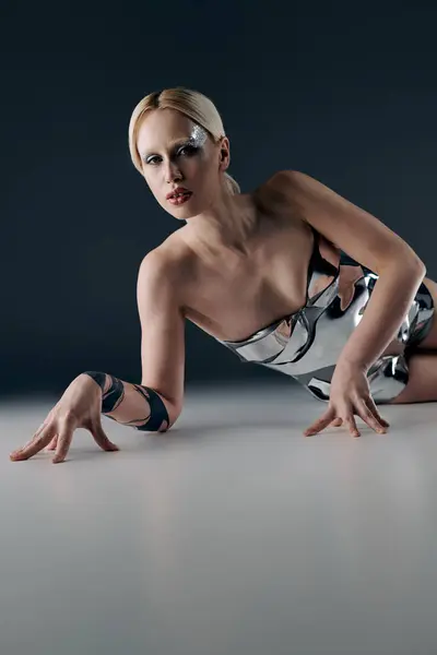Mujer extravagante en traje futurista plateado tumbado en el suelo y mirando a la cámara en el fondo negro - foto de stock