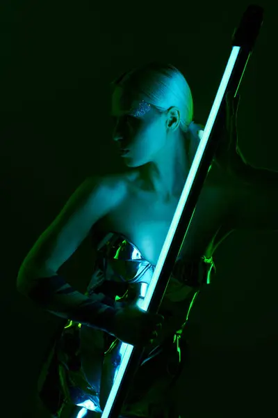 Mulher extraordinária em trajes robóticos metálicos segurando vara lâmpada LED azul e olhando para longe — Fotografia de Stock