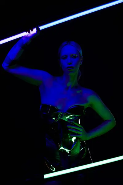Attraktive bizarre Frau in Roboterkleidung posiert mit blauem LED-Lampenstick und blickt in die Kamera — Stockfoto