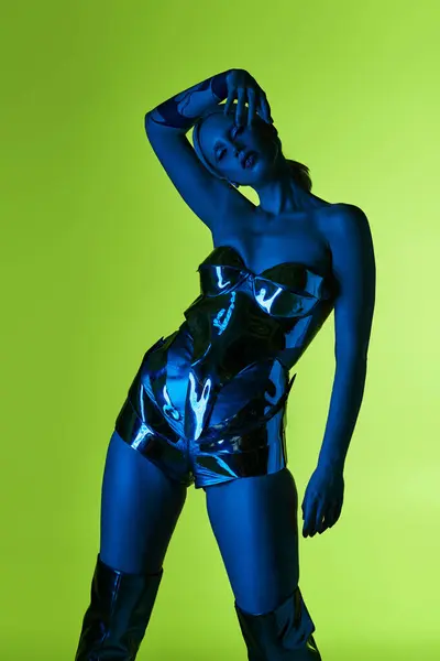 Mujer futurista en traje robótico posando en luces azules sobre fondo verde y mirando a la cámara - foto de stock