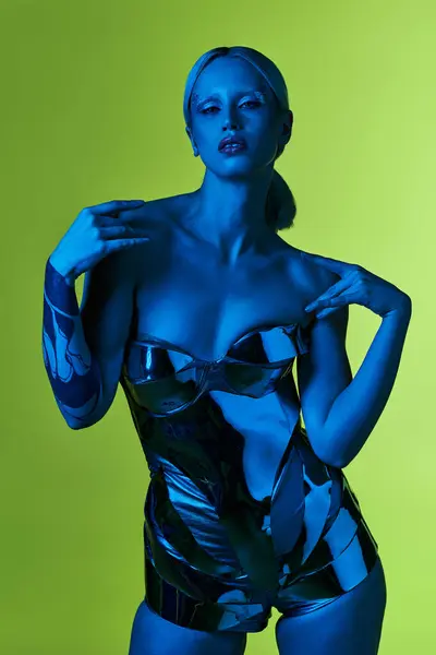 Außergewöhnliche Frau in Roboterkleidung posiert in blauem Licht vor grünem Hintergrund und blickt in die Kamera — Stockfoto