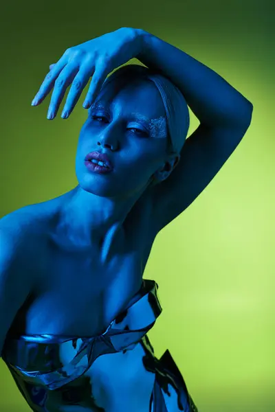 Extraordinaria mujer en traje robótico posando en luces azules sobre fondo verde y mirando a la cámara - foto de stock