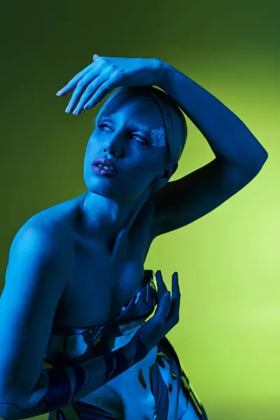 Peculiar attractive woman in futuristic sci fi attire posing in blue lights on green backdrop — Stock Photo