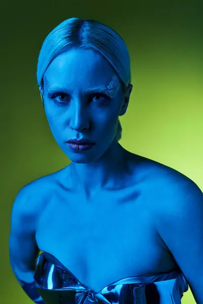 Extravagante Frau in Roboterkleidung posiert im Blaulicht vor grünem Hintergrund und blickt in die Kamera — Stockfoto