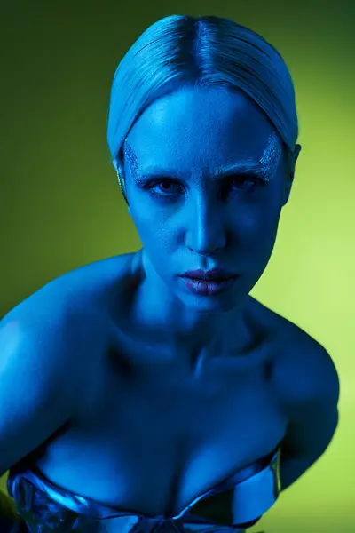 Екстравагантна жінка в робототехнічному одязі позує в синіх вогнях на зеленому тлі і дивиться на камеру — стокове фото