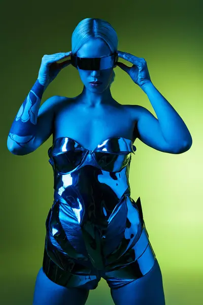 Mujer futurista en traje robótico plateado con gafas de sol de ciencia ficción posando en luces sobre fondo verde - foto de stock