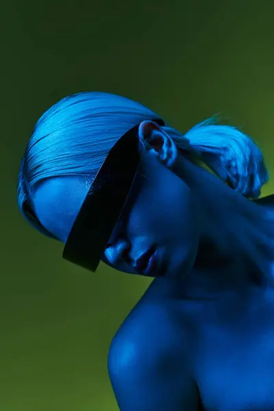 Экстравагантная блондинка в фантастических роботизированных солнцезащитных очках позирует в синих огнях на зеленом фоне — стоковое фото