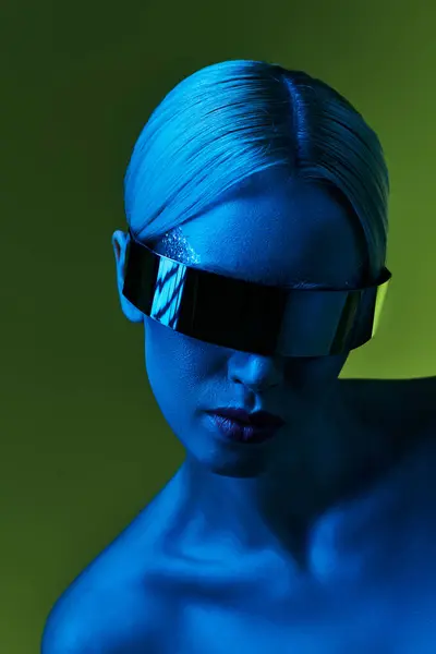 Extravagante blonde Frau mit Science-Fiction-Robotersonnenbrille posiert im Blaulicht vor grünem Hintergrund — Stockfoto