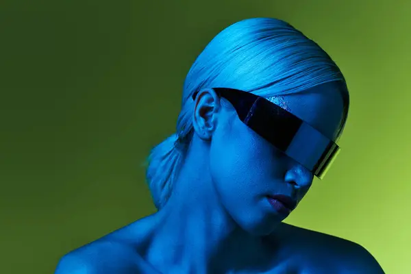 Außergewöhnliche blonde Frau mit Sci-Fi-Robotersonnenbrille posiert in blauem Licht vor grünem Hintergrund — Stockfoto