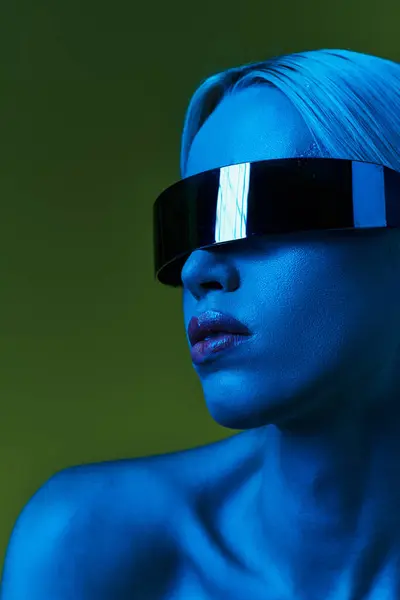 Extraordinary blonde woman with sci fi robotic sunglasses posing in blue lights on green backdrop — Stock Photo