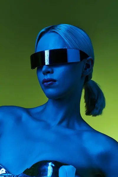 Mujer extravagante en traje robótico plateado con gafas de sol de ciencia ficción posando en luces sobre fondo verde - foto de stock