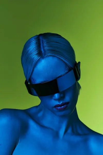 Futuriste blonde femme avec science-fiction robotique lunettes de soleil posant dans les lumières bleues sur fond vert — Photo de stock