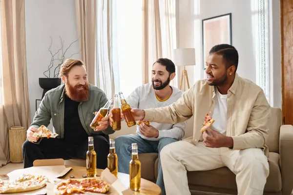 Três homens alegres e inter-raciais sentados em um sofá, desfrutando de pizza e cerveja em um ambiente casual em casa. — Fotografia de Stock