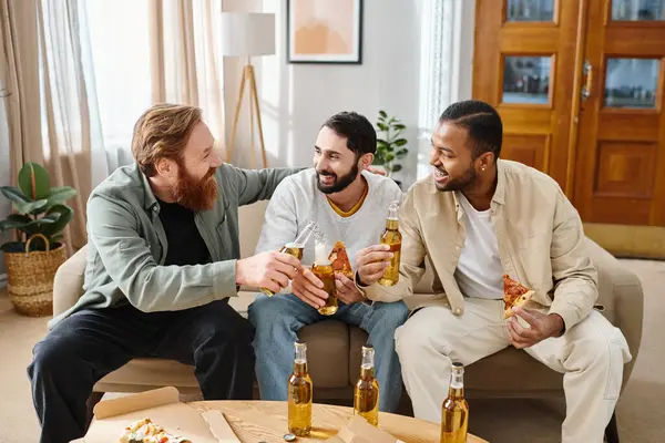Trois hommes heureux de différentes races dégustant de la bière et de la pizza sur un canapé en tenue décontractée, célébrant leur amitié. — Photo de stock