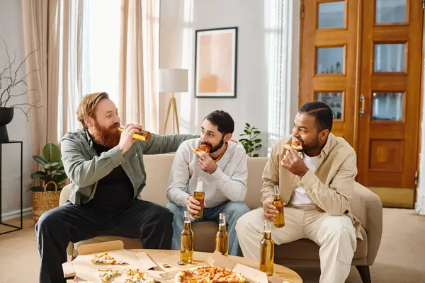 Trois beaux et joyeux hommes de différentes races assis sur un canapé, mangeant de la pizza et buvant de la bière, partageant des rires et de bons moments. — Photo de stock