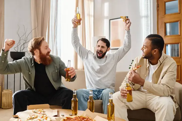 Trois beaux hommes de différentes races assis sur un canapé, dégustant de la bière et de la pizza dans un cadre confortable à la maison. — Photo de stock