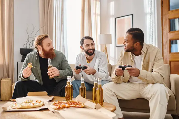 Трое веселых, красивых мужчин разных национальностей в повседневной одежде, сближаются за видеоиграми дома. — стоковое фото