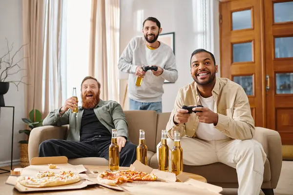 Trois hommes joyeux, de races différentes, riant et jouant à des jeux vidéo sur un canapé en tenue décontractée, profitant d'un moment amusant ensemble. — Photo de stock