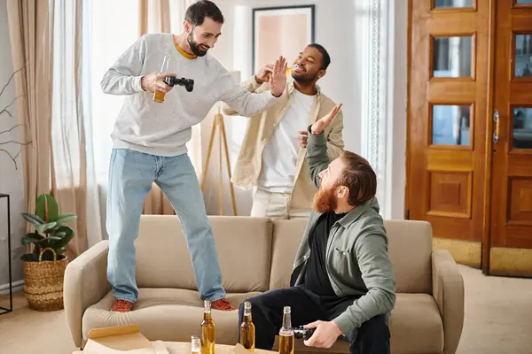 Two cheerful men stand on top of a couch, while another man watches, exuding joy and friendship in casual attire. — Stock Photo