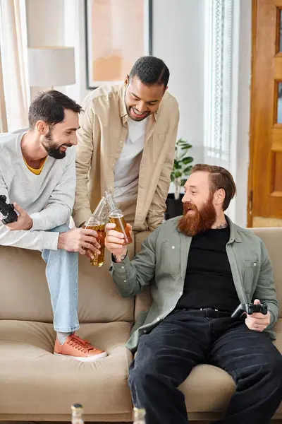 Three cheerful, interracial men in casual attire, bonding and having a great time together on a couch at home. — Stock Photo