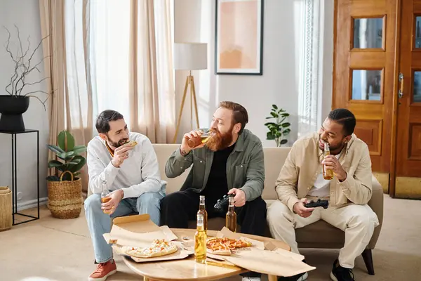 Trois hommes gais et interracial en tenue décontractée dégustant pizza et bière sur un canapé, exprimant amitié et camaraderie. — Photo de stock