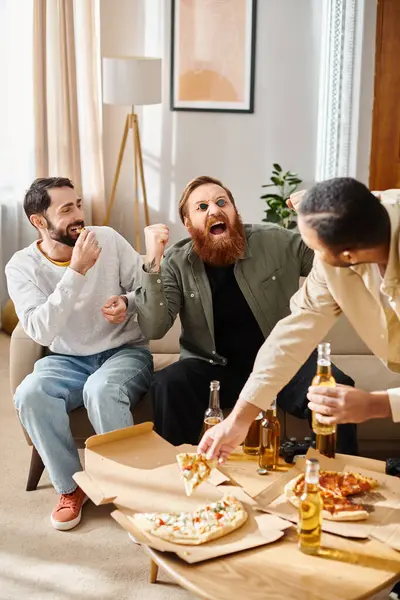 Trois hommes joyeux et beaux de différentes races dégustent une pizza autour d'une table dans un cadre confortable à la maison. — Photo de stock
