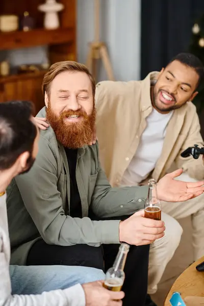 Tres hombres alegres y guapos de diferentes razas disfrutan de bebidas y conversaciones alrededor de una mesa en atuendo casual, exudando calidez y amistad. - foto de stock