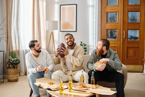Tres hombres alegres, interracial en atuendo casual disfrutando de pizza juntos alrededor de una mesa en un ambiente acogedor. - foto de stock