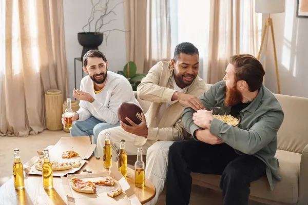 Tres hombres elegantes y diversos comparten alegremente pizza y cerveza en un acogedor sofá en casa. - foto de stock