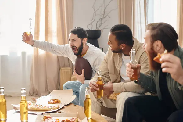 Trois hommes joyeux et beaux de différentes races s'assoient autour d'une table, dégustant des pizzas et se tenant compagnie dans un cadre confortable à la maison. — Photo de stock