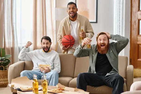 Tres hombres alegres y guapos de diferentes razas disfrutando de la compañía de los demás en un acogedor sofá en casa. - foto de stock