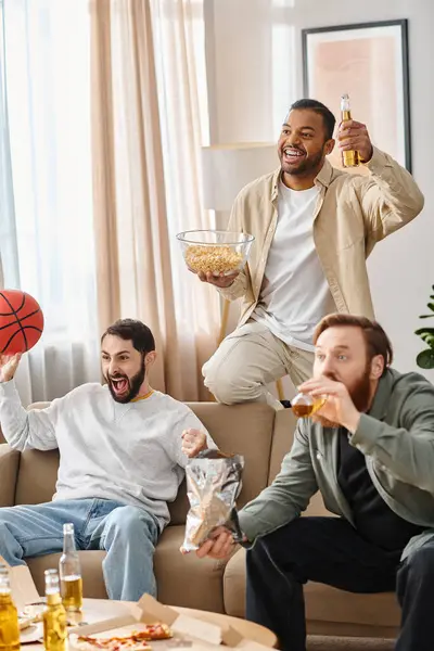 Three cheerful men of different races sit atop a couch, enjoying slices of pizza in a cozy home setting. — Stock Photo