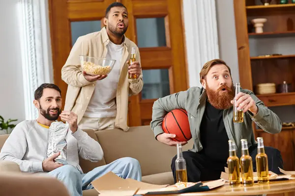 Tre uomini belli interrazziale in abbigliamento casual condividere bevande, ridere, e godersi un grande momento insieme a casa. — Foto stock