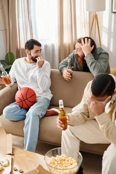 Tres hombres alegres e interraciales en atuendo casual se sientan encima de un sofá acogedor, compartiendo risas y compañía. - foto de stock