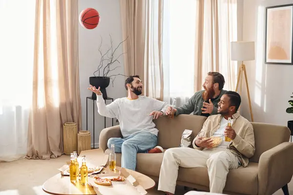 Three handsome men of different races sit happily and relax on top of a couch in a casual home setting. — Stock Photo