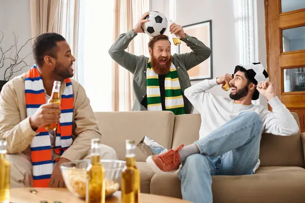Três homens alegres, de etnias variadas, compartilhando um momento animado em cima de um sofá em trajes casuais. — Fotografia de Stock