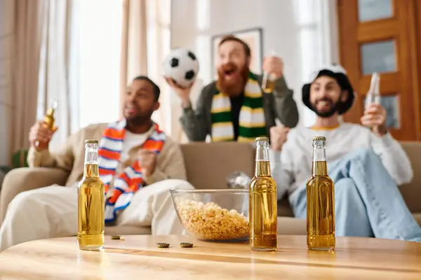 Un grupo de tres hombres interraciales y alegres con atuendo casual se sientan de cerca en un sofá, inmersos en ver la televisión juntos. - foto de stock