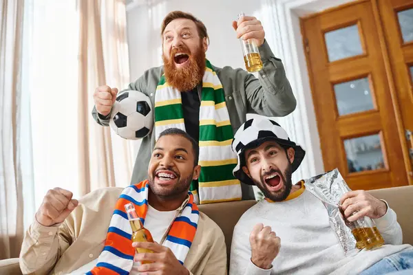 Three handsome, cheerful, interracial friends sitting atop a couch, enjoying each others company in a casual setting at home. — Stock Photo