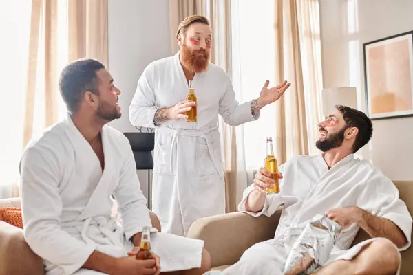 Three diverse, cheerful men in bathrobes relax and bond on top of a couch, sharing laughter and camaraderie. — Stock Photo