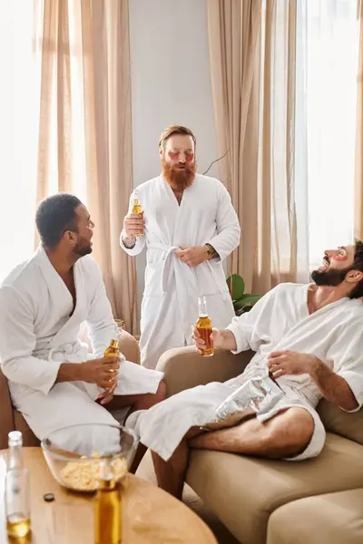 Three diverse, cheerful men in bathrobes enjoy each others company in a cozy living room setting. — Stock Photo