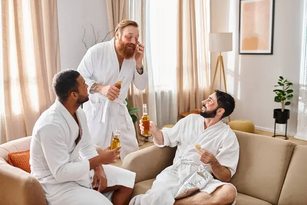 Трое мужчин в белых халатах комфортно сидят на диване, наслаждаясь компанией друг друга и разделяя моменты дружбы. — стоковое фото