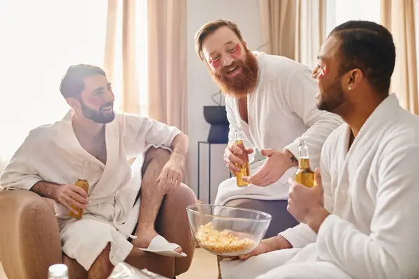 Three diverse, cheerful men in bathrobes sitting on top of a couch, enjoying each others company. — Stock Photo