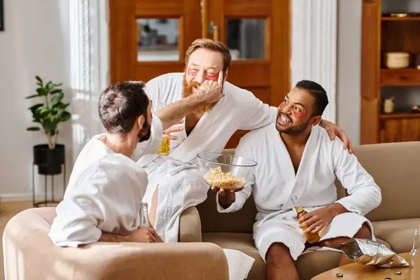 Three cheerful men in bathrobes enjoy a cozy moment on top of a couch, showcasing the essence of friendship and camaraderie. — Stock Photo