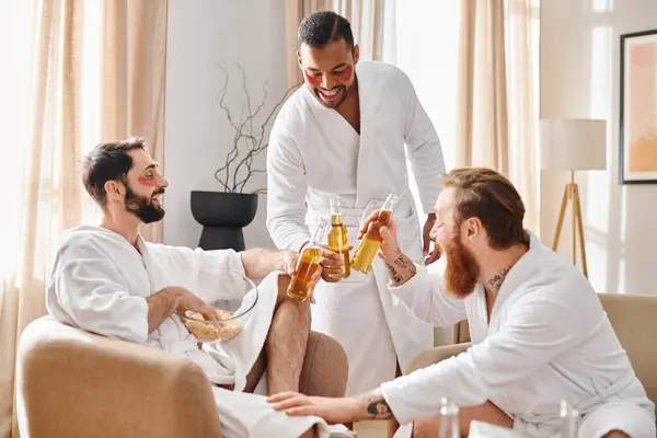 Three diverse, cheerful men in bathrobes chatting and laughing in a cozy living room. — Stock Photo